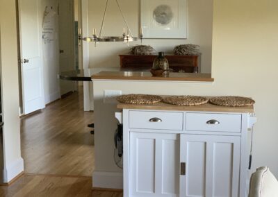 A well-lit interior scene featuring a portable kitchen island on hardwood flooring with a view into an adjoining room.