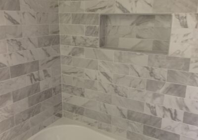 A modern bathroom featuring a bathtub with marble-patterned wall tiles and a built-in niche for toiletries.