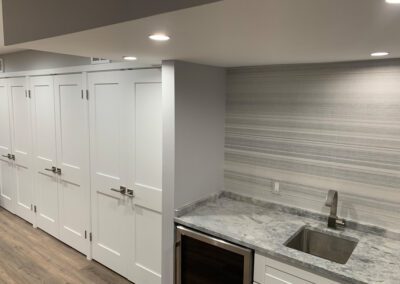 Modern kitchen with white cabinets, stainless steel handles, gray backsplash, and marble countertops.