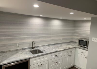 Modern kitchen with marble countertops and gray striped backsplash under white cabinetry.