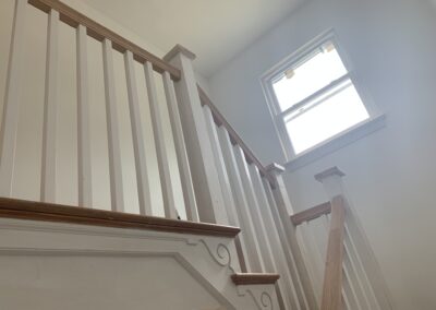 Interior view of a staircase with wooden banisters, leading upwards towards a small window letting in daylight.