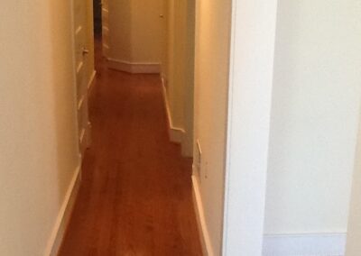 A narrow residential hallway with wooden flooring and white walls.