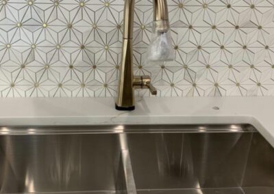 Stainless steel double sink with a gold-toned faucet against a geometric tile backsplash.