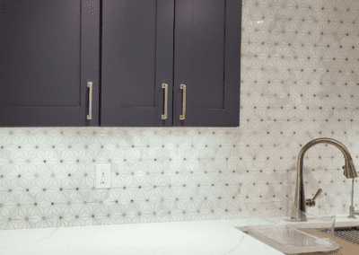 Modern kitchen interior with dark cabinetry and geometric backsplash.