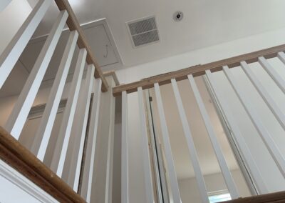 Wooden staircase with white balusters and a handrail, viewed from the bottom looking up.