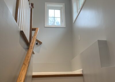 A stairwell with wooden banisters and steps leading upwards, illuminated by natural light from a window at the top.