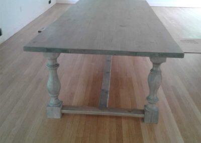 A wooden table with turned legs on a hardwood floor in an empty room with a fireplace.