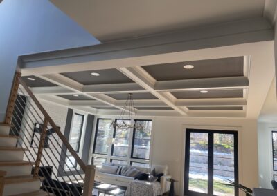 Modern living room with coffered ceiling, pendant lights, and a staircase with metal balusters.