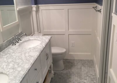 A clean and modern bathroom with white wainscoting, a double vanity, and a patterned tile floor.