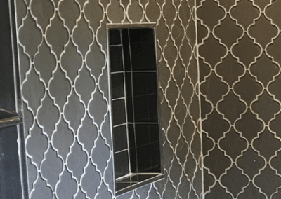 A shower with gray patterned tiles and built-in shelving.