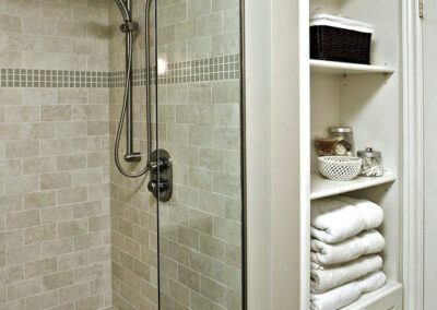 A neatly organized bathroom corner featuring a glass shower stall and shelving with towels and toiletries.