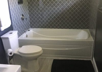 Modern bathroom interior with a white bathtub, toilet, and dark tiling.