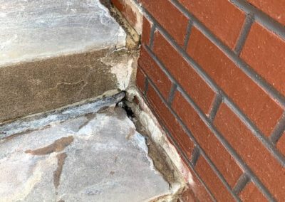 Weathered concrete steps showing signs of deterioration next to a brick wall.