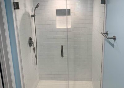 Modern walk-in shower with glass doors and white subway tiles.