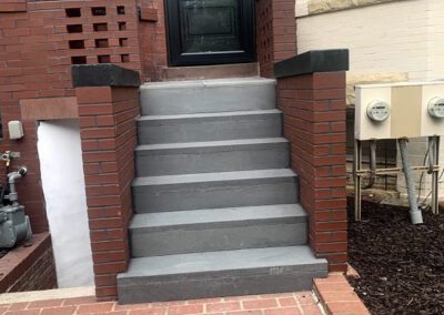 Entrance to a building with a red brick facade, featuring a gray concrete staircase and a black door with the number 80.