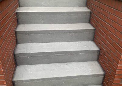 A flight of grey painted concrete steps flanked by red brick walls.