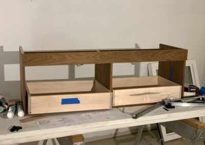 Partially assembled wooden furniture with open drawers on a workbench, surrounded by tools and construction materials.