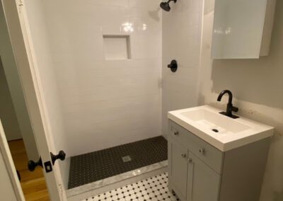 A small, modern bathroom with white subway tiles, black and white floor tiles, a white sink vanity, and black fixtures.