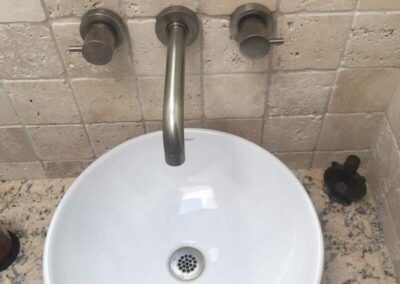 A white basin with a single lever faucet flanked by two control knobs, set against a tiled backsplash.