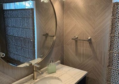 Modern bathroom with herringbone tile walls, round mirror, and a marble countertop sink.