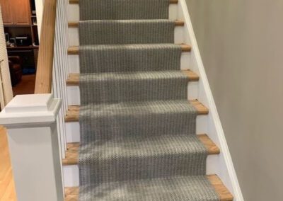 Staircase with wooden steps and grey herringbone-patterned carpet runner.