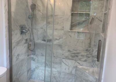 A modern bathroom featuring a marble-tiled walk-in shower with glass doors next to a white toilet.