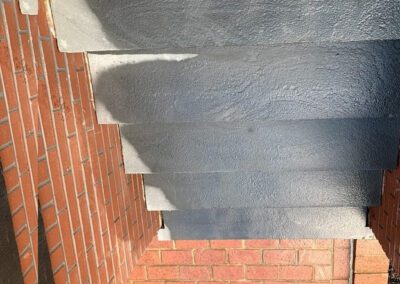 Concrete steps with a metal railing against a red brick background, viewed from above.